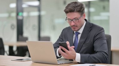 Ofiste akıllı telefon kullanan orta yaşlı bir iş adamı. 