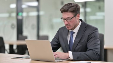 Odaklanmış Orta Çağ İşadamı Ofiste Dizüstü bilgisayar üzerinde çalışıyor 