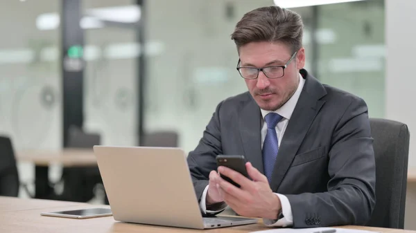 Moyen Age Homme d'affaires travaillant sur ordinateur portable et Smartphone au bureau — Photo