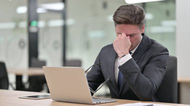 Dizüstü bilgisayarı olan orta yaşlı iş adamı ofiste baş ağrısı çekiyor 