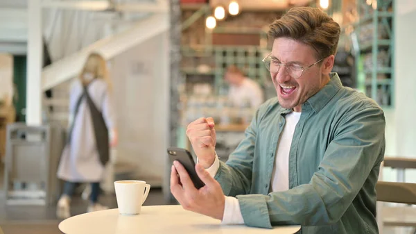 Homme du Moyen Âge Célébration du succès sur Smartphone à Cafe — Photo