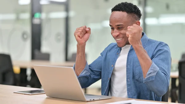 Casual African Man Celebrating Success on Laptop in Office