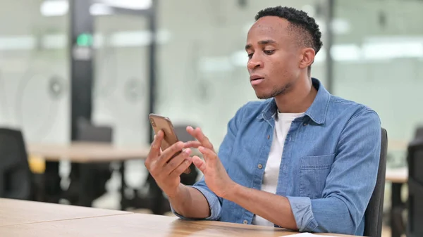 Fokuserad avslappnad afrikansk man med hjälp av smartphone i Office — Stockfoto