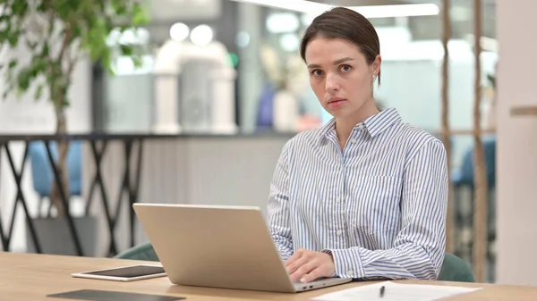 Seriös ung kvinna med bärbar dator tittar på kameran — Stockfoto