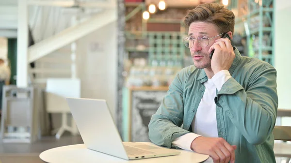 Medelålders man med bärbar dator talar på telefon i Café — Stockfoto