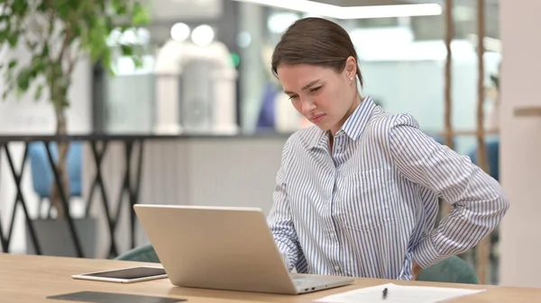Dizüstü bilgisayarlı yorgun genç kadın ofiste sırt ağrısı çekiyor. — Stok fotoğraf