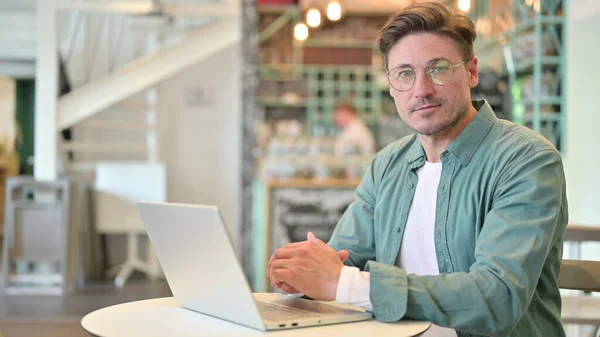 Hombre serio de mediana edad con ordenador portátil mirando a la cámara —  Fotos de Stock