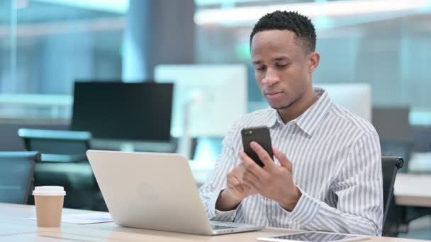 Uomo d'affari africano con computer portatile utilizzando Smartphone al lavoro — Video Stock