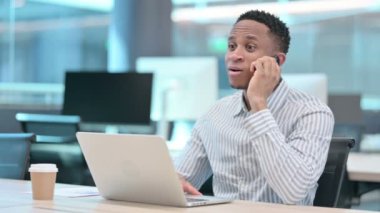 Dizüstü bilgisayarlı kızgın Afrikalı İşadamı Akıllı Telefonla konuşuyor 