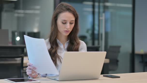 O tânără femeie de afaceri cu un laptop care citește documente la locul de muncă — Videoclip de stoc