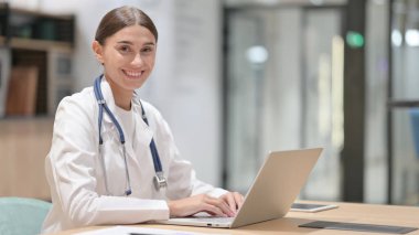 Ofiste gülümseyen dizüstü bilgisayarı olan arkadaş canlısı kadın doktor. 