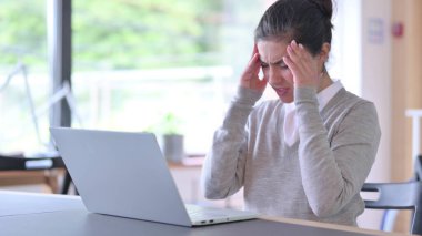 Dizüstü bilgisayarı olan stresli genç Hintli kadının işte başı ağrıyor.