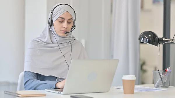 Kulaklıklı genç Arap kadın dizüstü bilgisayarda çalışıyor.