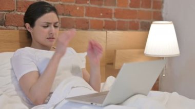 Yatakta dizüstü bilgisayarla uğraşırken baş ağrısı çeken genç Hintli kadın.