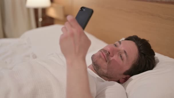 Mężczyzna w średnim wieku za pomocą smartfona podczas snu w łóżku — Wideo stockowe