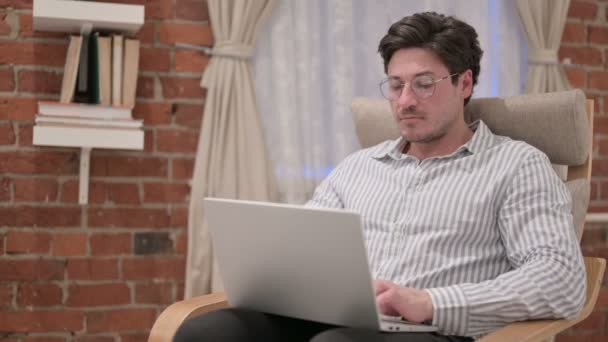 Középkorú férfi laptoppal a kanapén lévő kamerára mutat — Stock videók