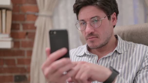 Портрет мужчины средних лет, реагирующего на потерю на смартфоне — стоковое видео