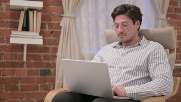 Hombre de mediana edad con el ordenador portátil sacudiendo la cabeza como sí en el sofá — Vídeos de Stock