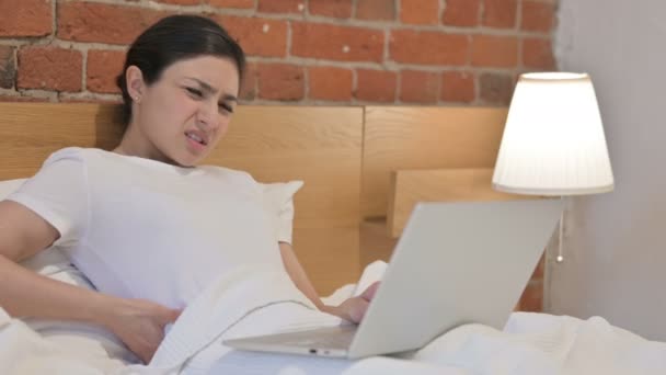 Junge Inderin mit Rückenschmerzen arbeitet im Bett am Laptop — Stockvideo