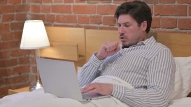 Laptoplu orta yaşlı adam yatakta öksürüyor.