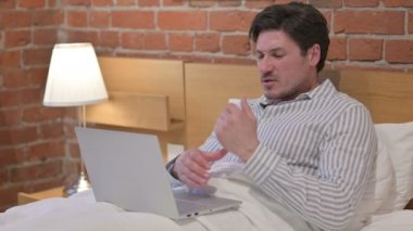 Orta yaşlı adam bilek ağrısı çekiyor, laptopla yatakta çalışıyor.