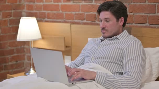Мужчина средних лет празднует успех на ноутбуке в постели — стоковое видео