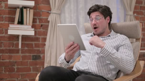 Мужчина средних лет празднует успех на планшете на диване — стоковое видео