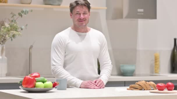 Человек улыбается перед камерой, стоя на кухне — стоковое видео