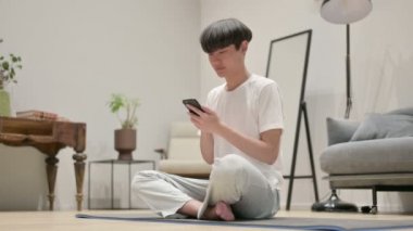Evde Yoga Matat 'ta akıllı telefon kullanan Asyalı adam.