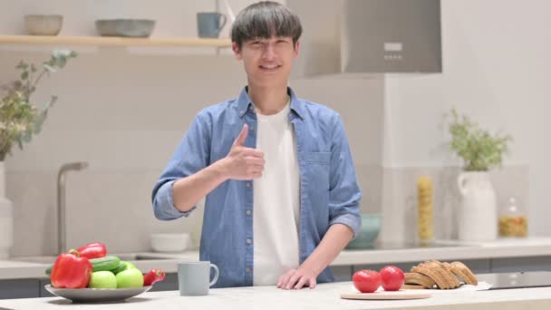 Asiatisk man visar tummen upp när du står i köket — Stockvideo