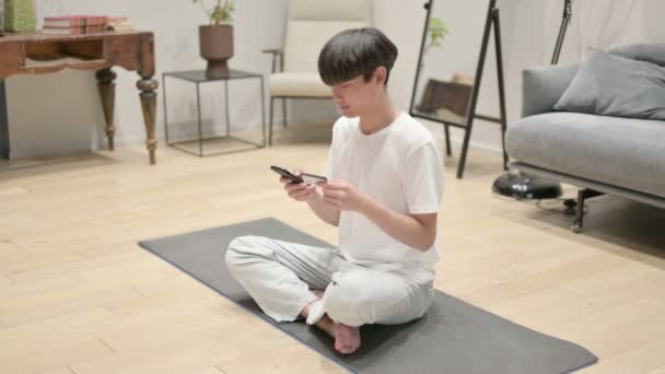 Hombre asiático haciendo pago en línea en Smartphone en Yoga Mat — Vídeos de Stock