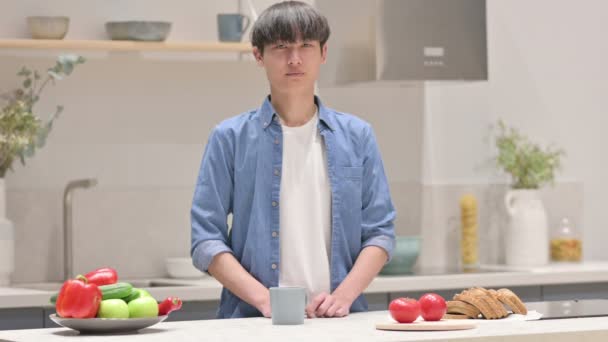 Asiático hombre mirando a la cámara mientras de pie en cocina — Vídeos de Stock