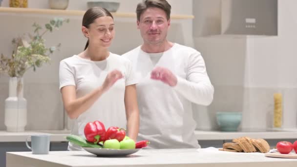 Pareja de raza mixta haciendo forma de corazón por manos en la cocina — Vídeo de stock