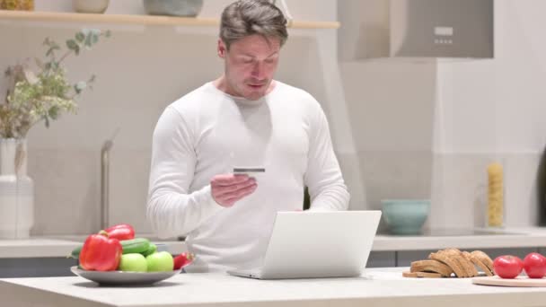 Hombre haciendo el pago en línea en el ordenador portátil en la cocina — Vídeo de stock