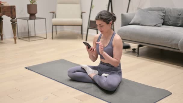 Femme indienne utilisant Smartphone sur tapis de yoga à la maison — Video