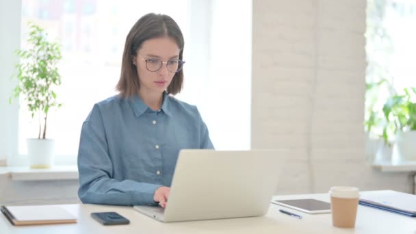 Mujer joven mirando a la cámara mientras usa el ordenador portátil en la oficina — Vídeo de stock