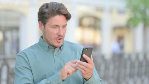Mann mittleren Alters feiert im Freien auf Smartphone — Stockvideo
