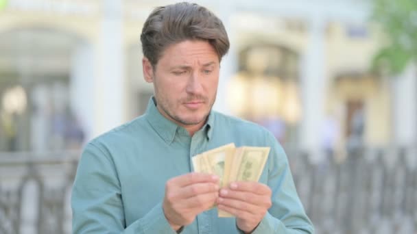 Porträt eines Mannes mittleren Alters, der Dollars im Freien zählt — Stockvideo