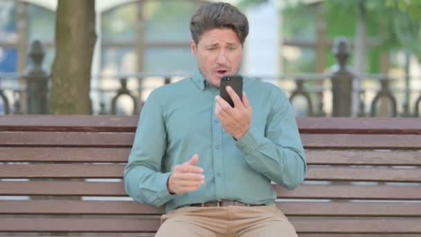 Расстроенный мужчина средних лет реагирует на потерю на смартфоне — стоковое видео