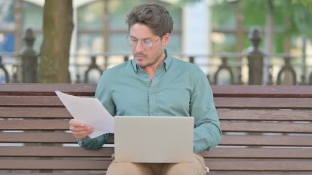 Pomyślny średniowieczny człowiek Czytanie dokumentów podczas korzystania z laptopa — Wideo stockowe