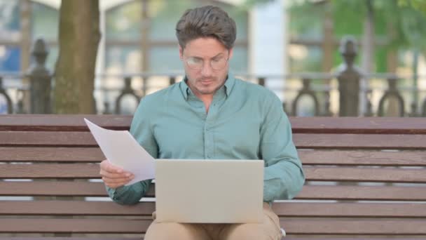 Molesto hombre de mediana edad lectura de documentos mientras se utiliza el ordenador portátil — Vídeo de stock