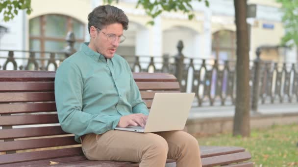 Чоловік відчуває здивованість під час використання ноутбука на лавці — стокове відео