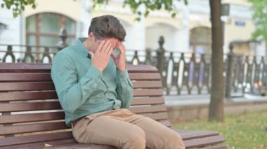 Bir adam bankta otururken kızgın hissediyor. 