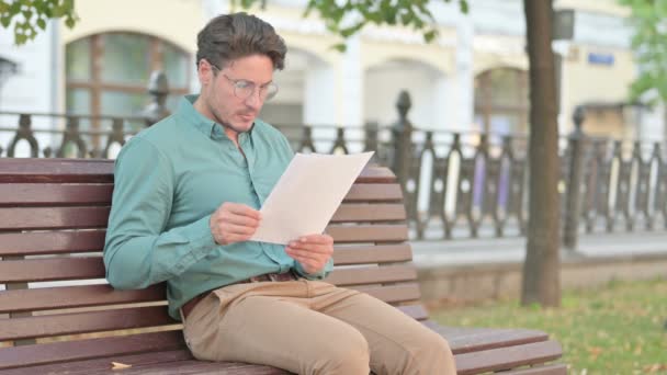 Man die documenten leest terwijl hij op de bank buiten zit — Stockvideo