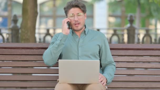 Homem de meia-idade falando no telefone enquanto estiver usando laptop — Vídeo de Stock
