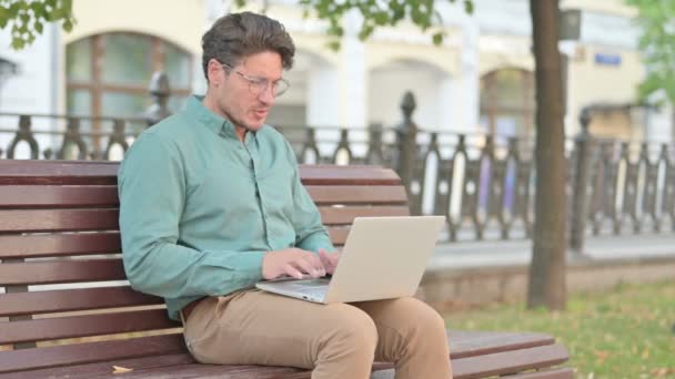 Человек с болями в спине во время использования ноутбука на скамейке — стоковое видео