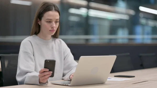 Mujer usando Smartphone mientras trabaja en Laptop —  Fotos de Stock