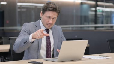 Bilgisayarlı orta yaşlı iş adamı kamerayı işaret ediyor.