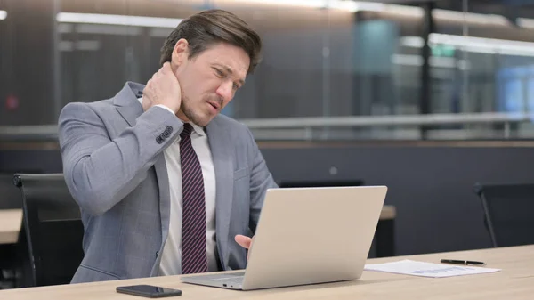 Dizüstü bilgisayarı olan orta yaşlı iş adamı ofisinde boyun ağrısı çekiyor. 