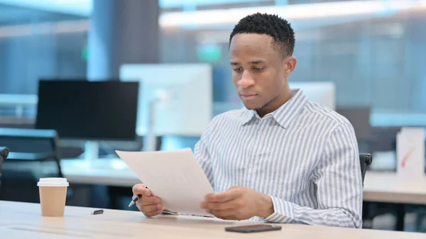 Afrikanischer Geschäftsmann liest Dokumente im Amt — Stockfoto